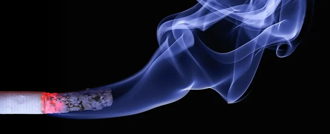 Gros plan sur une cigarette consumée avec des volutes de fumée sur fond noir, illustration principale pour arrêter de fumer avec l'hypnose